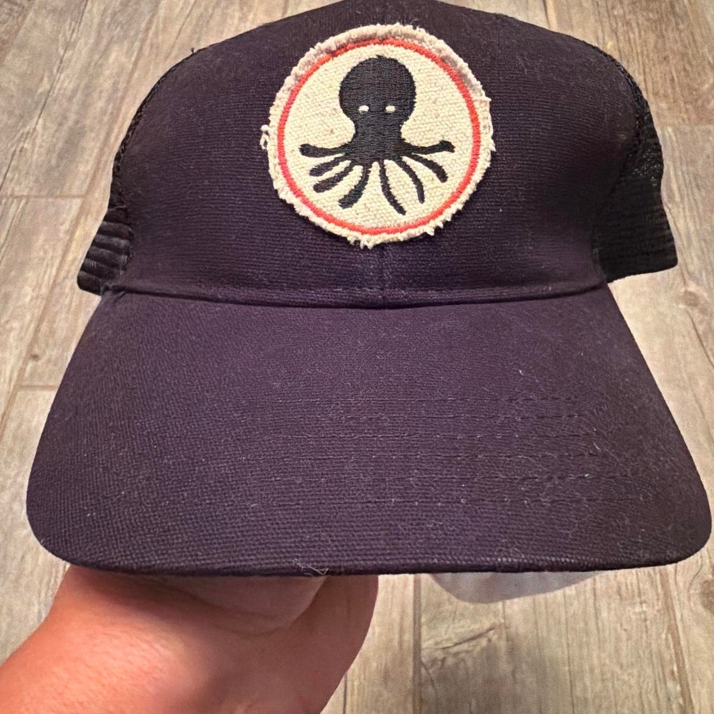 Black trucker cap with black octopus graphic on a cream background